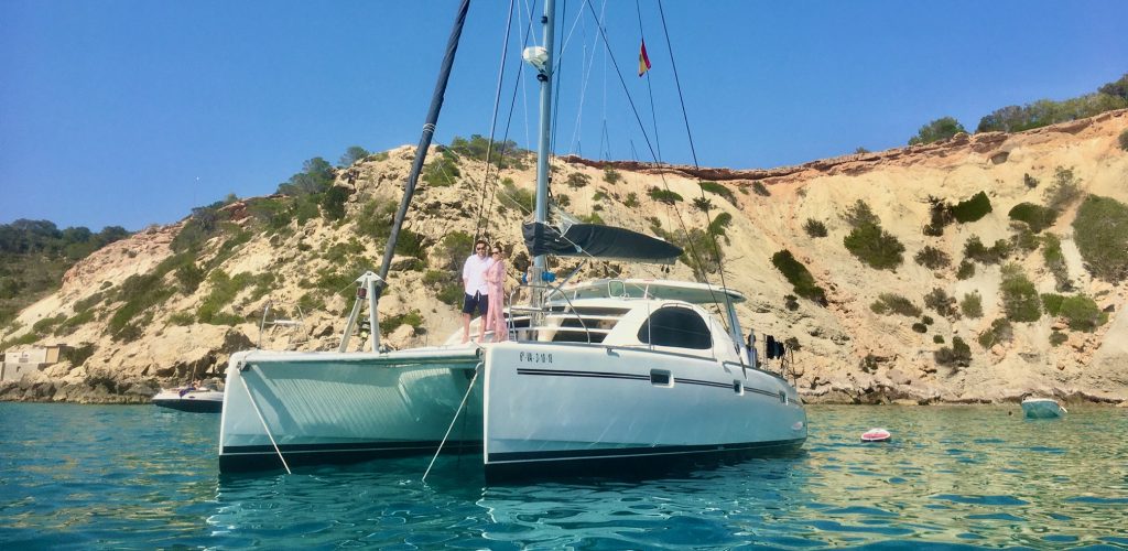 pareja posando en la red de nuestro catamarán fondeado en las aguas de Ibiza.