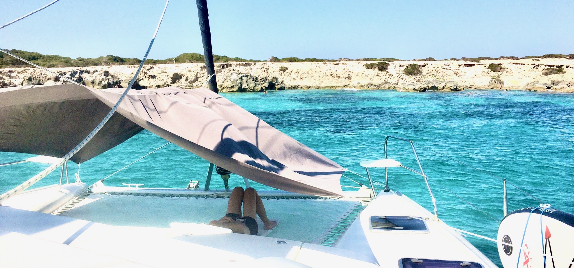 Louez un catamaran à Ibiza pour une journée, client allongé sur le filet devant le parc naturel de Salinas.