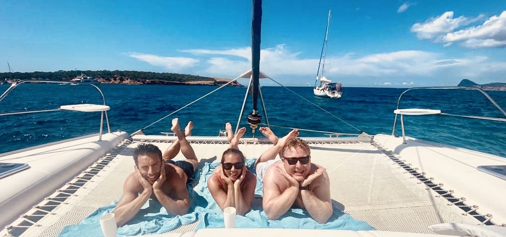 Alquiler barco Ibiza, tres amigos tumbados en la red de nuestro catamaran