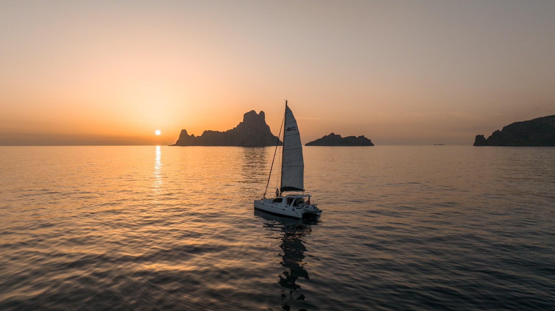 The couple at the bow of the catamaran while the sun sets in Es Vedra